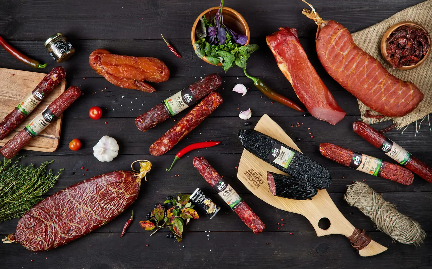 Ассортимент полукопчёных и варёно-копчёных колбас «Дело Вкуса» на тёмном деревянном фоне